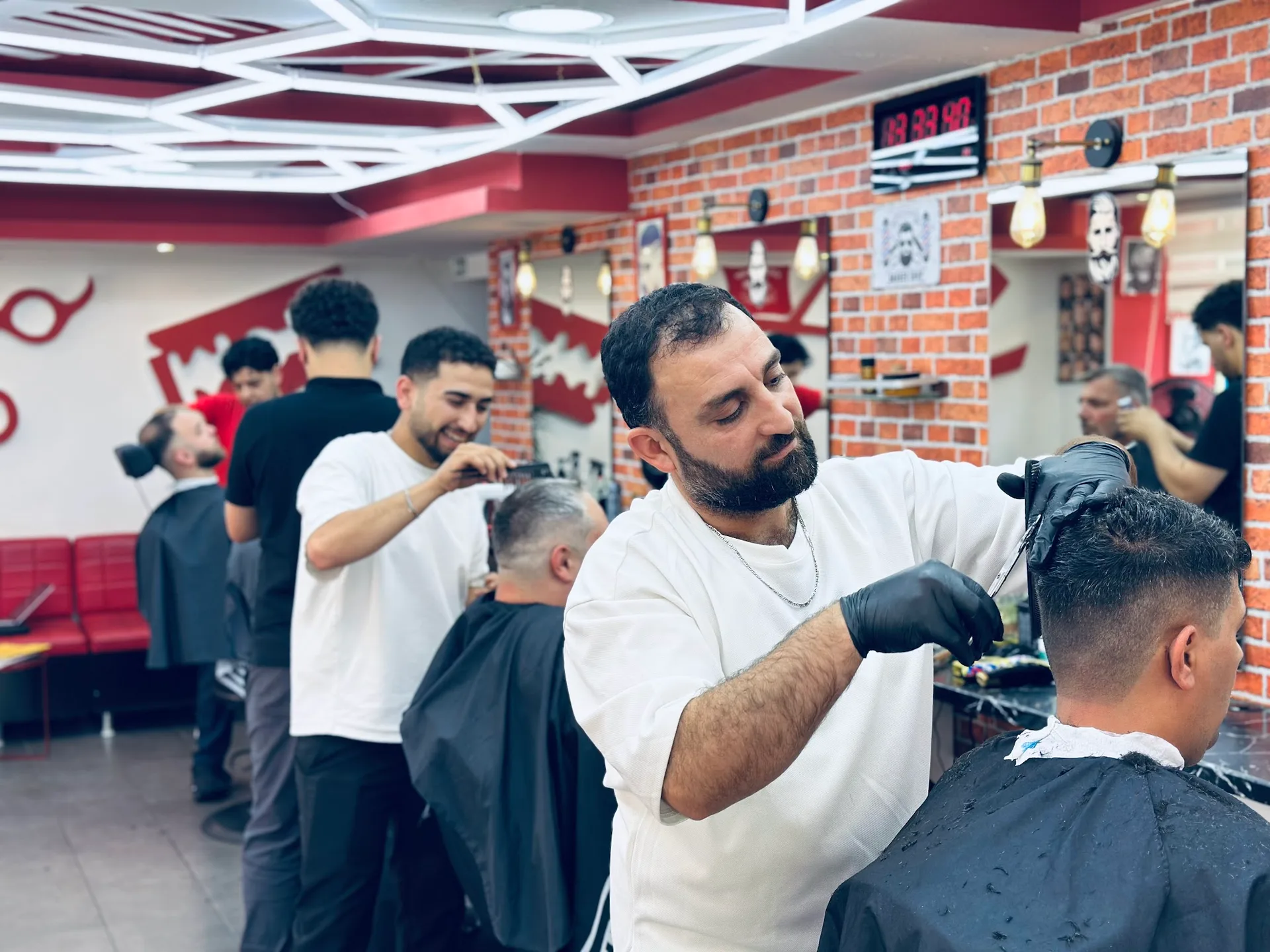 Voller Salon des Ster Barber Shop: vier Barbiere arbeiten gleichzeitig, Ziegelwände, Wabendecke und rote Wartebank
